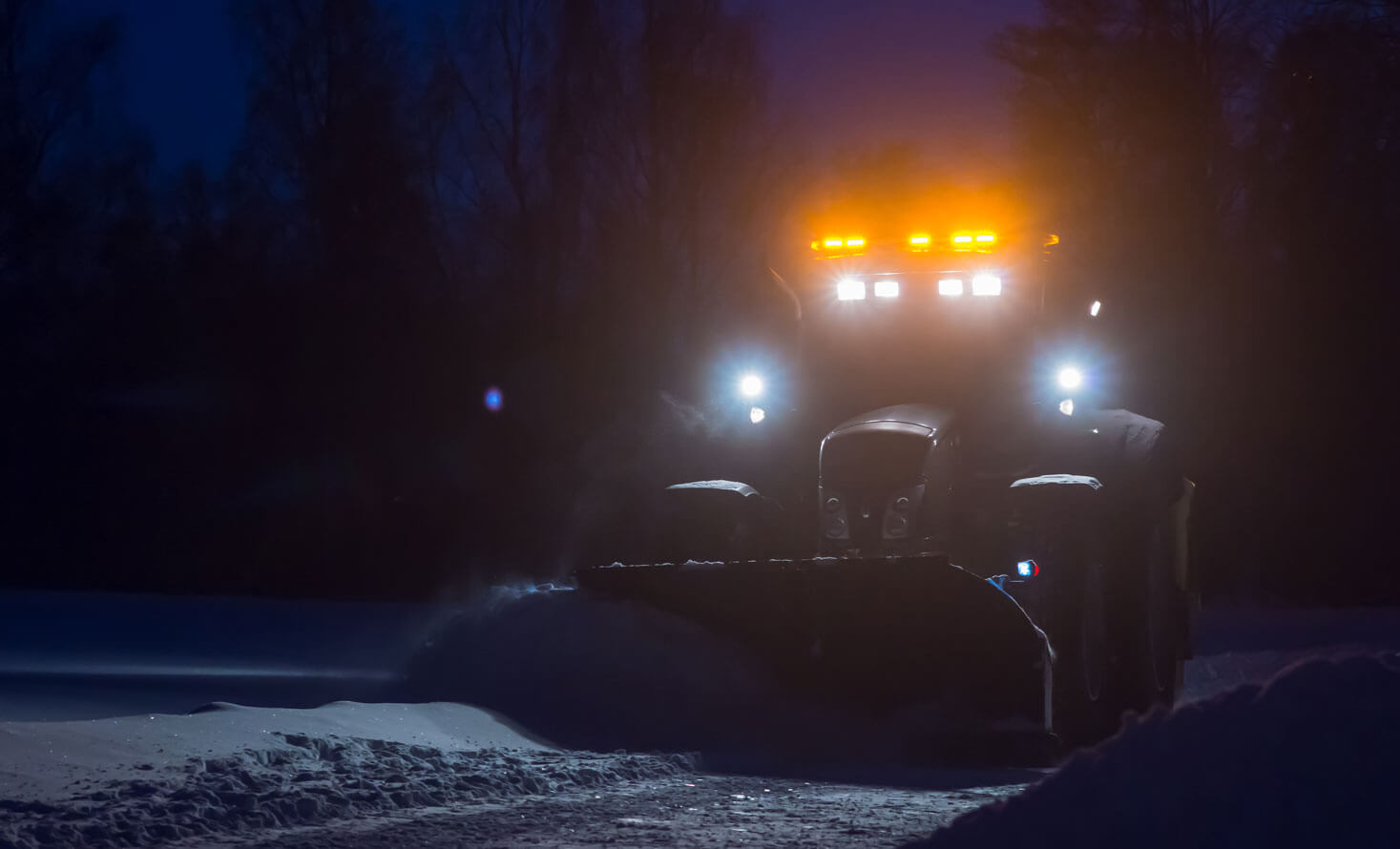 Traktor som brøyter i mørke med kraftige arbeidslys og varsellys