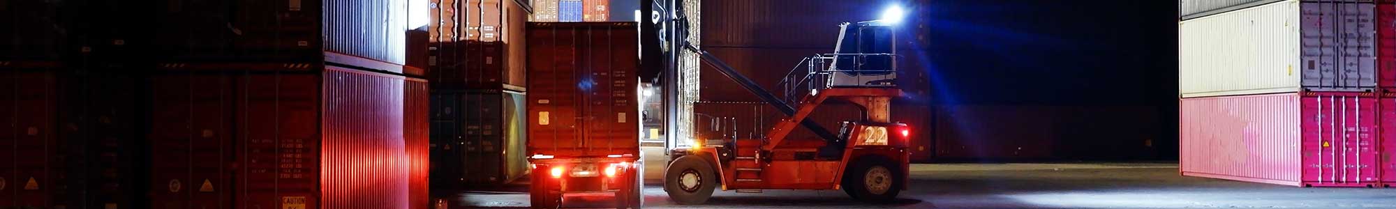 Truck som flytter containere i en mørk havn med scenebelysning og arbeidslys